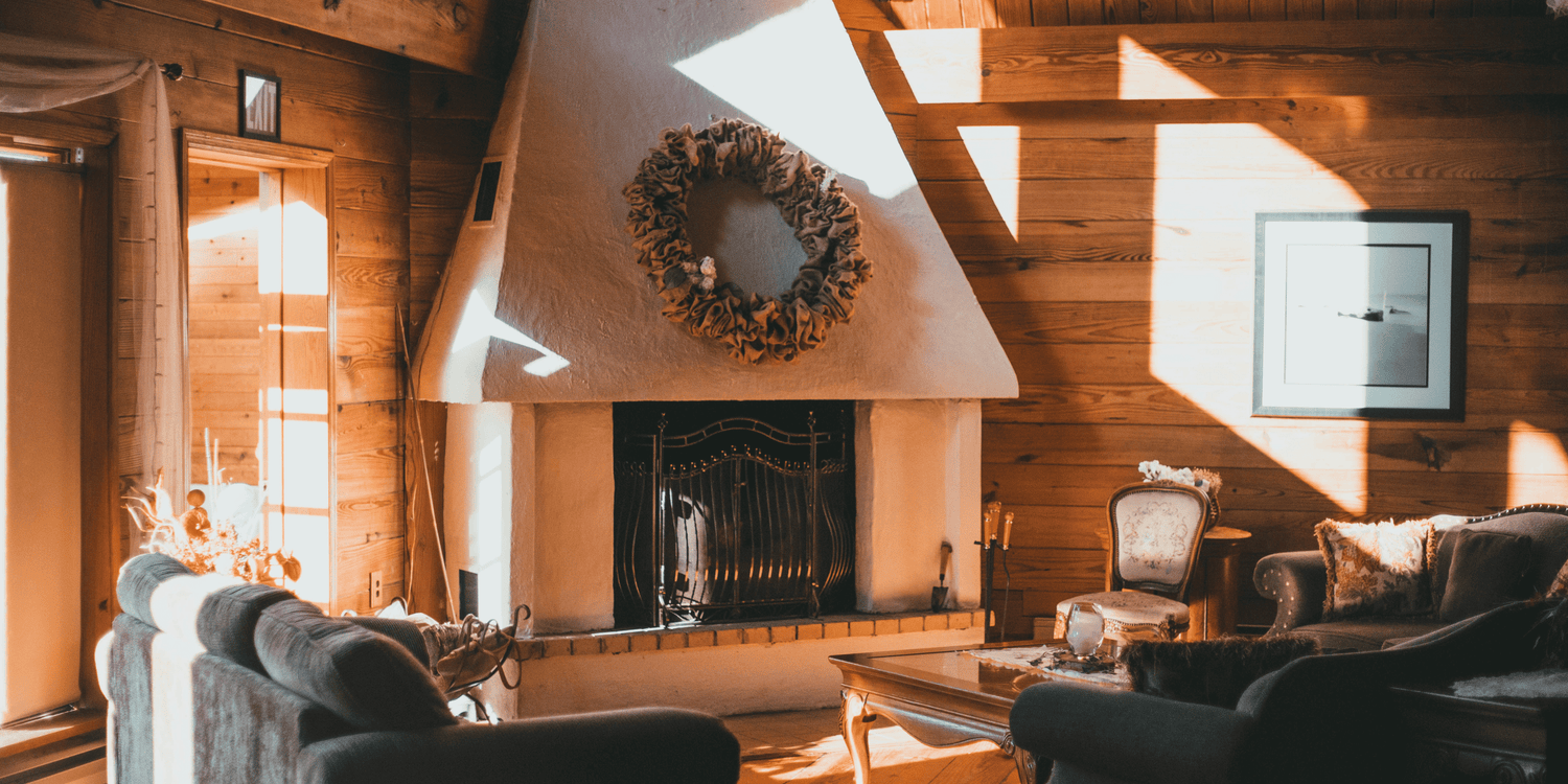 Warm rustic living room with wooden walls, cozy furniture, and a fireplace decorated with a wreath